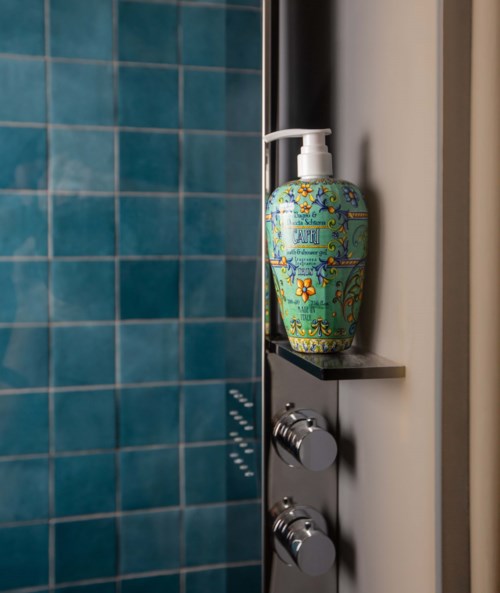 Ein dekorativer Seifenspender auf einem Regal neben einer Dusche mit blauen Fliesen.
