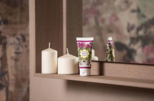 Ein Regal mit zwei Kerzen und einer Tube Handcreme neben einem Spiegel in einem gemütlichen Raum.