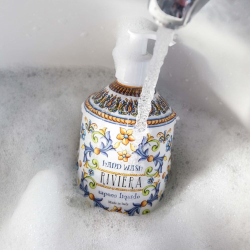 Eine dekorative Seifenspender mit der Aufschrift 'Hand Wash Riviera' unter fließendem Wasser im Waschbecken.