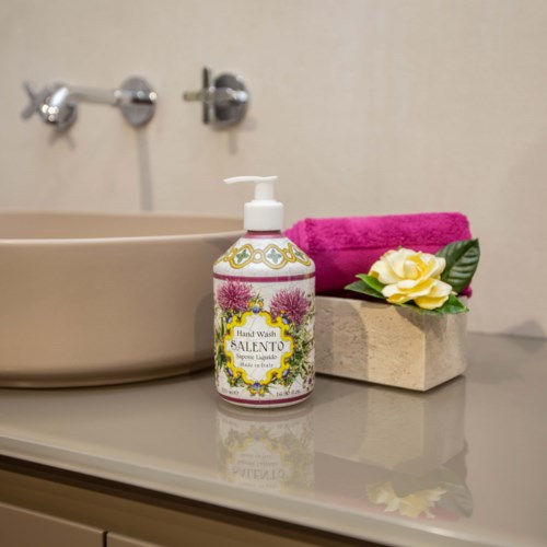 Eine Flasche Handseife, ein rosa Handtuch und eine Blume in einer kleinen Steinschale auf einer Badezimmertheke.