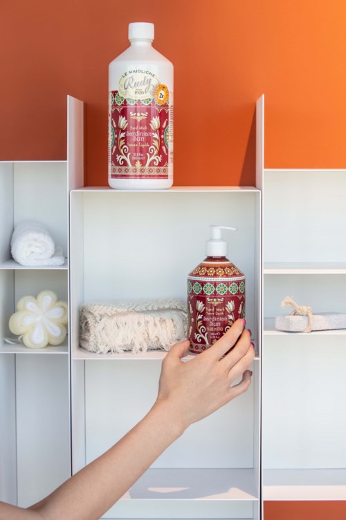 To flasker shampoo og body wash på en hvid hylde med håndklæder og en svamp.