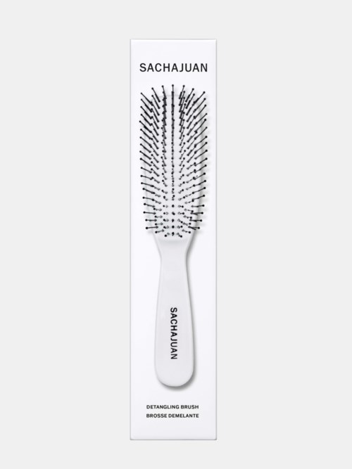 A white detangling hairbrush with the brand name 'SACHAJUAN' on the handle, shown in an illustration with packaging.