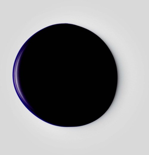 Musta ympyräinen objekti, jossa on himmeä violetti hohde vaaleanharmaalla taustalla.