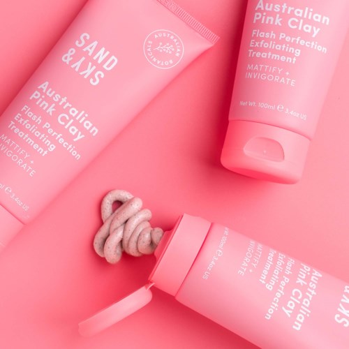 Rosa hudpleieprodukter, tube og flaske, med en krøllet krem eller skrubb som kommer ut, på rosa bakgrunn.