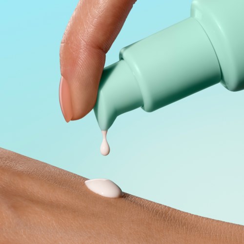 En hånd påfører lotion eller krem på huden med en tube, mot en lys blå bakgrunn.