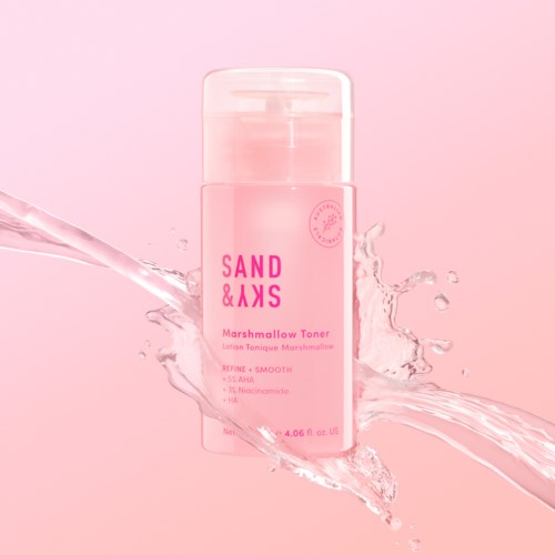 Lyserosa flaske med marshmallow toner og vannskvett, merket 'SAND & SKS', på rosa bakgrunn.