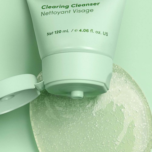 A green tube of face cleanser, partially squeezed, with some gel squeezed out on a flat surface.