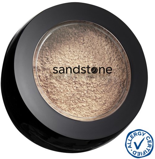 En rund makeup-behållare med beige puder och ordet 'sandstone' inuti. Den har ett svart lock och en allergivarningsstämpel.