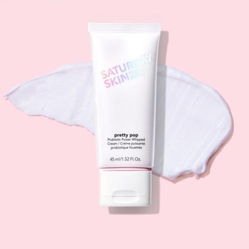 Eine weiße Tube mit Hautpflegecreme, Pink- und Lilatext, auf pinkem Hintergrund mit Creme.