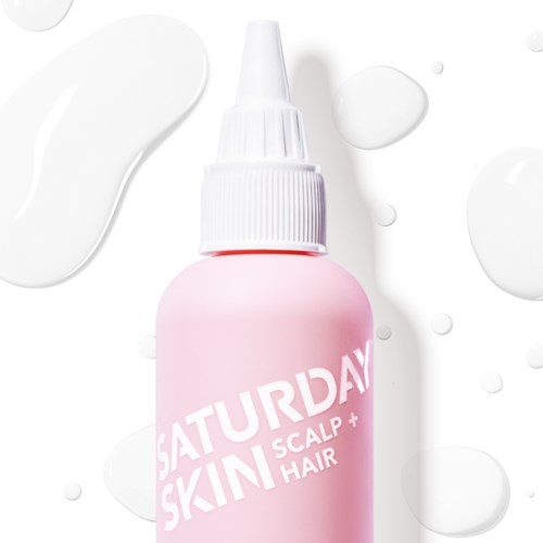 Ruusukupillin valkoinen suutin merkitty "Saturday Skin Scalp + Hair". Se on asetettu valkoiselle taustalle, jossa on tippoja.