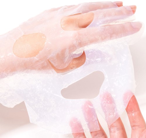 En hand håller ett vitt ansiktsmaskark med utskärningar för ögon, näsa och mun.