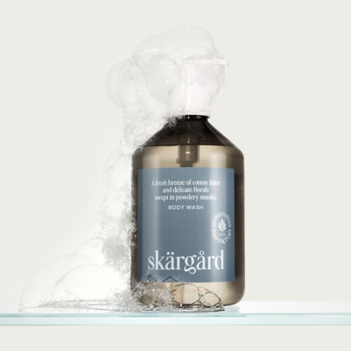 Een donker flesje met lichtblauw label, dat schuim en bellen afgeeft, met de naam Skärgård body wash.