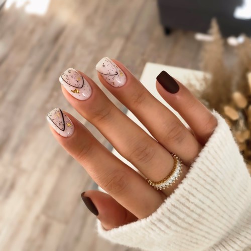 Neglene er pyntet med hvid polish, sorte streger, guld prikker og glimmer. Hånden har en ring og en cremefarvet sweater.