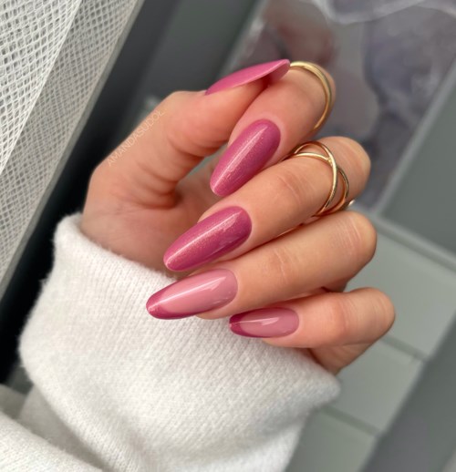 En hånd med lange rosa negler og flere gullringer, iført en hvit genser, vises nært.