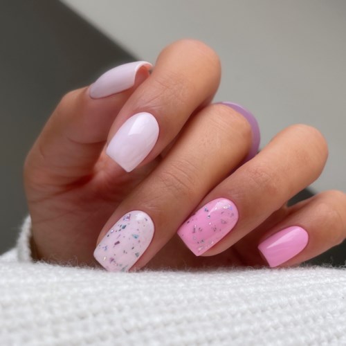 Hånden har rosa og hvite negler med glitter og prikker, et morsomt negldesign.