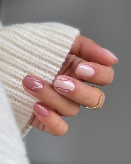 A hand with well-manicured nails in pink and white, wearing a gold ring and a cream sweater.