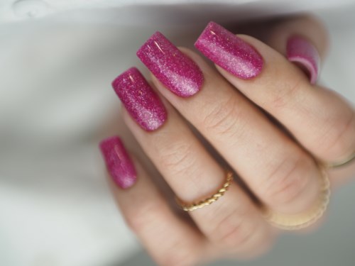 Nærbilde av en hånd med lange rosa glitternegler og ringer på fingrene.