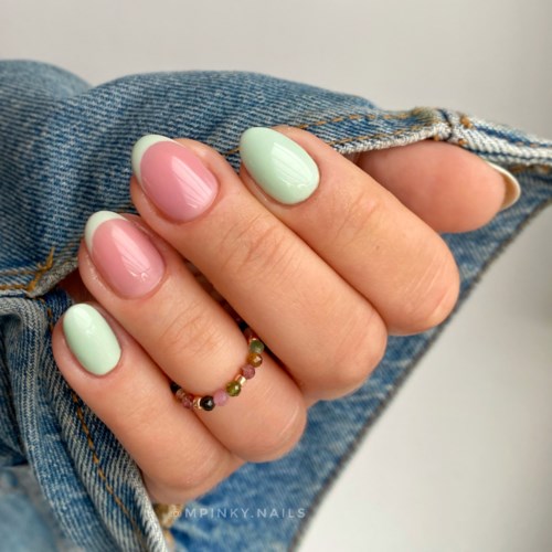 Negle malet i pink og grøn, med en guldring med små farvede sten, holdt foran denim stof.