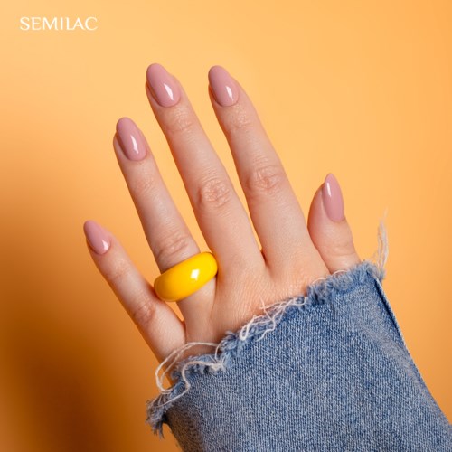 En hånd med lyserøde negle og en gul ring, iført en slidset blå denimærme, mod en ferskenbaggrund.