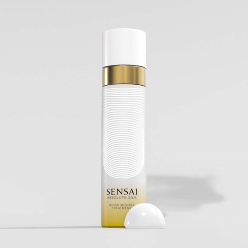 En vit cylindrisk flaska med ett guldband, märkt 'SENSAI Absolute Silk Micro Mousse Treatment', står på en plan yta.