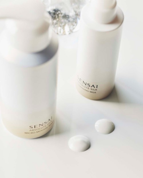 Två vita flaskor med svart text, en med spray, och två klickar av vit kräm eller lotion.