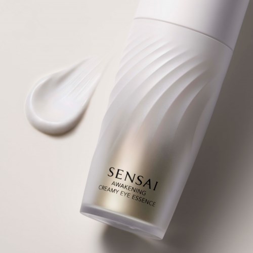 En vit flaska med Sensai Awakening Creamy Eye Essence och övrig kräm bredvid.
