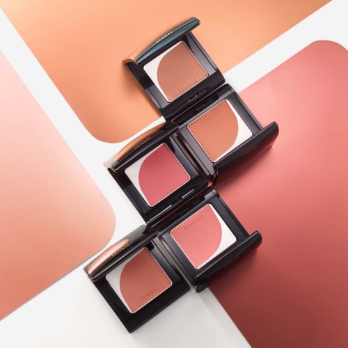 Three blush compacts with shades of pink and peach, open on a pink, peach, and white background.