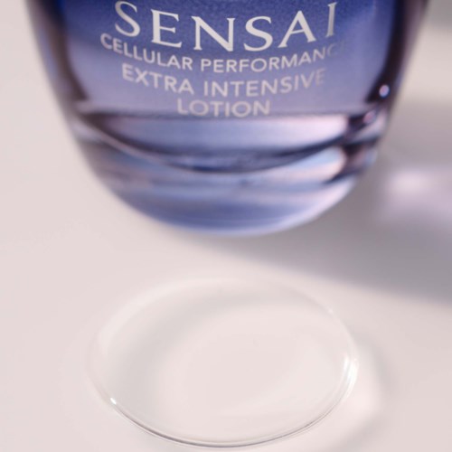 En blå flaska Sensai-lotion med klart liquid, placerad på en vit yta.