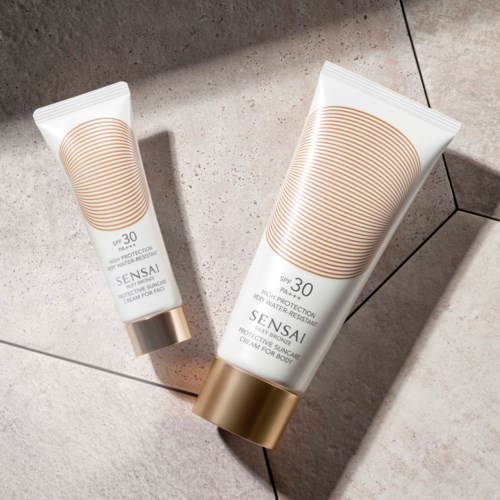 Två flaskor med solkräm med guldlock placerade på kaklad yta, en stor och en liten, märkta SPF 30.