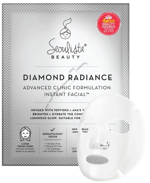 En hvit ansiktsmaske foran en sølvfarget eske merket 'Diamond Radiance' for avansert hudpleie, med en liten rød enamring øverst til høyre.