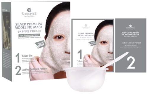 Boks med ansiktsmasker, en børste, en skål og bilder av en kvinne som bruker ansiktsmaske. Den promoterer et hudpleieprodukt.