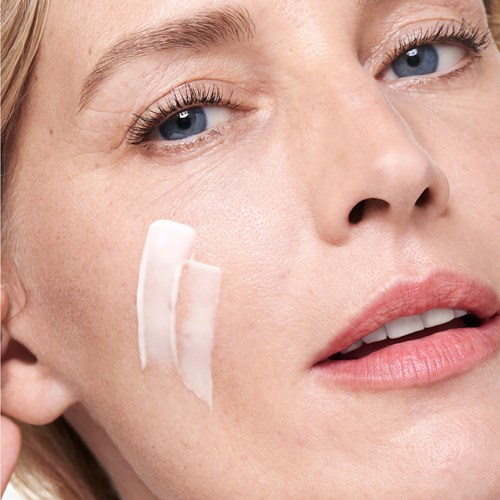 Close-up of a woman applying or removing skin cream on her face, with clear skin and light makeup.
