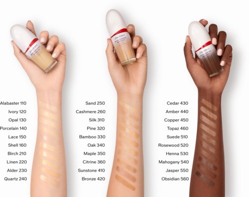 Three hands hold foundation bottles with color names and swatches visible on skin. The bottles are labeled and have different shades.
