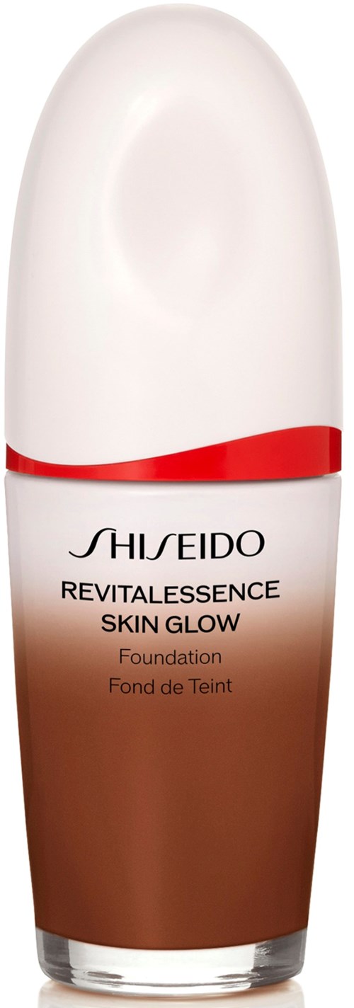 En foundationflaske med hvit og brun design, rød linje og svart tekst. Den er fra Shiseido's Revitalessence Skin Glow-serie.