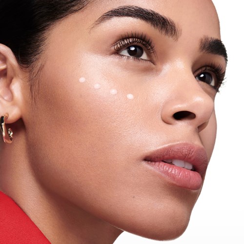 A woman applies skincare cream under her eyes with three small dots on her face.
