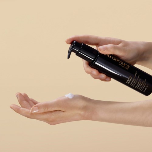 Eine Person gibt weiße Creme aus einer schwarzen Pumpflasche in die Hand.