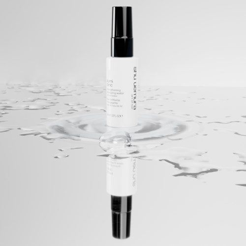 Eine weiße Sprühflasche mit schwarzem Deckel steht auf einer reflektierenden Oberfläche mit Wasserwellen.