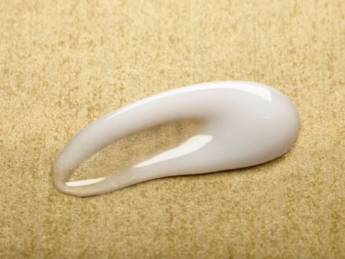 En klick vit kräm eller lotion på en beige yta, formad i en kurvig form med en glänsande yta.
