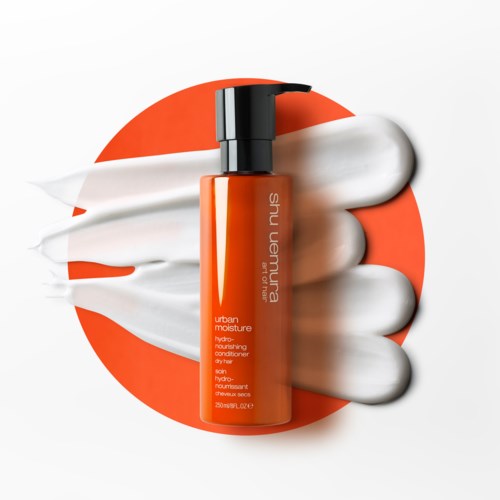 En flaska med Shu Uemura Urban Moisture Balsam med vit kräm runt den och en orange bakgrund.