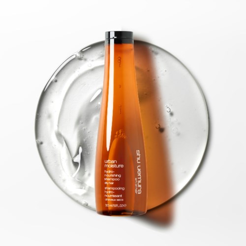 En orange schampoflaska märkt 'urban moisture' placerad på en reflekterande yta med vattenstänk runt den.