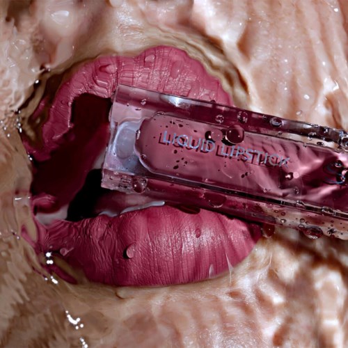 En person slickar rosa läppstift med ett genomskinligt läppglansbehållare i närheten.