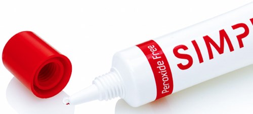Een witte tube met rode tekst, gelabeld 'Peroxide Face' en 'SIMPLE', een rode dop en een kleine druppel.