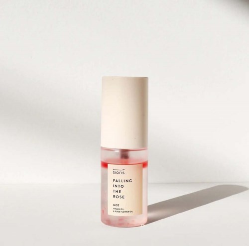 A small pink spray bottle with a white cap, labeled "Falling Into the Rose," standing on a white surface.