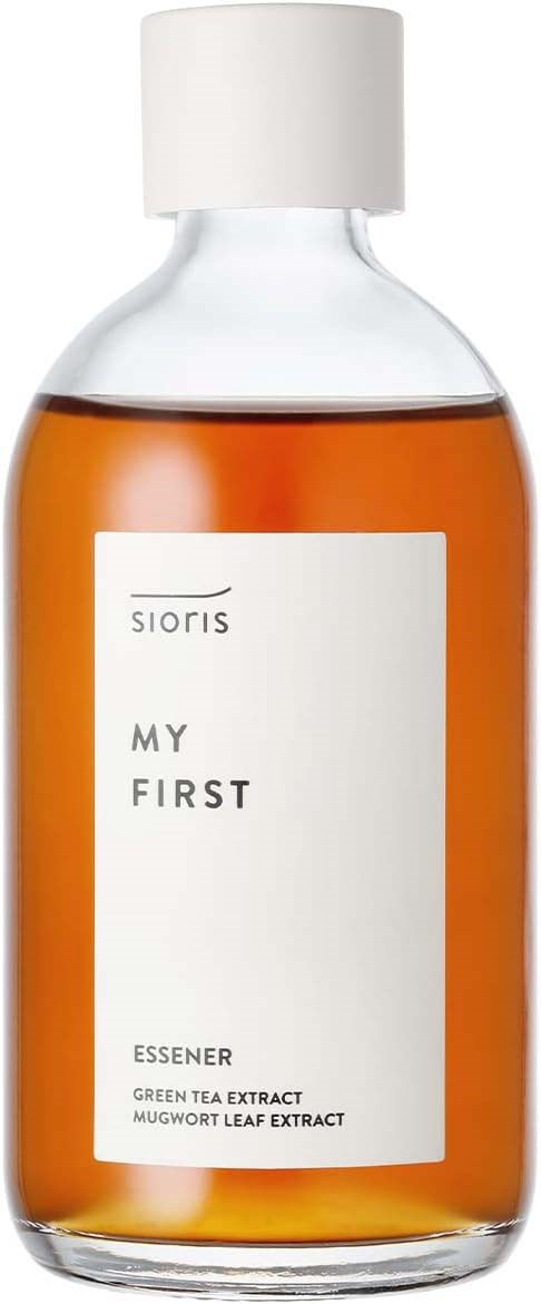 En klar glassflaske med oransje væske og hvit lokk, merket 'Sioris My First' med grønn te og mugwortbladekstrakt.