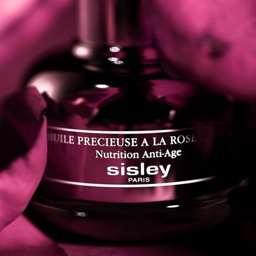 En mørk pink flaske mærket 'Sisley Paris' med ordene 'Essential Rose Oil' og 'Anti-Age Nutrition'.