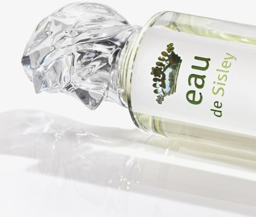 En glasflaska med en grön etikett ligger på sidan, med klar parfym som spillts ut. Etiketten säger "eau de Sisley."