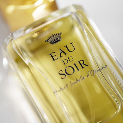 En parfymeflaske merket 'Eau du Soir' med gullfarge og elegant skrift, plassert på en myk bakgrunn.