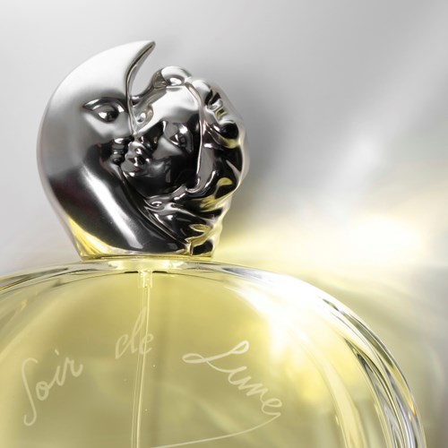 En parfume flaske med en sølvmåne og ansigt design på toppen, kaldet 'Soin de Lumie' med gul væske indeni.