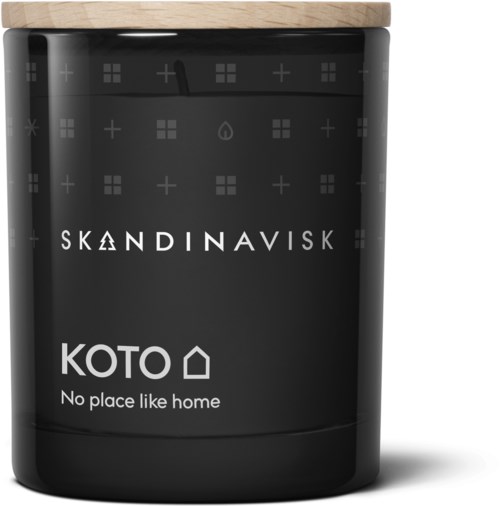 Een zwarte kaars met een houten deksel. Het label zegt "KOTO" en "No place like home." Op de kaars staan de tekst en merknaam.