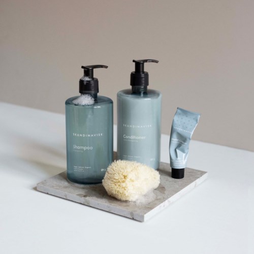 To blå flasker mærket shampoo og balsam, en lille tube og en svamp på en marmordisk.